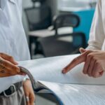Accounts Management - Colleagues Standing in White Long Sleeve Shirts Discussing and Reading a Financial Report