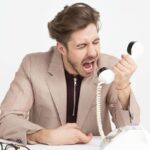 Spam Filters - Man Wearing Brown Suit Jacket Mocking on White Telephone